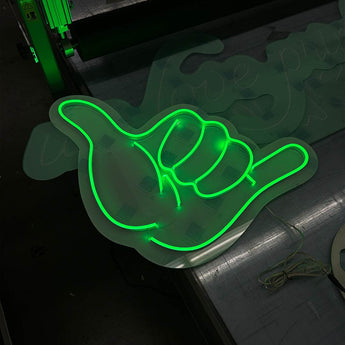 Grün leuchtendes LED Neon Schild in Form einer Shaka-Hand auf Acrylglas. Maßgeschneiderte Leuchtwerbung für Events.