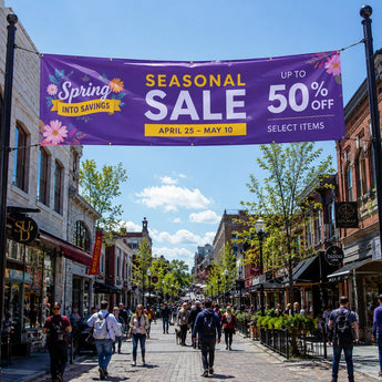 PVC Werbebanner in leuchtendem Lila mit der Aufschrift „Seasonal Sale“, das über eine belebte Einkaufsstraße gespannt ist. Das Banner ist wetterfest, verfügt über Metallösen zur Aufhängung und wirbt für eine Frühlingsaktion mit bis zu 50 % Rabatt.