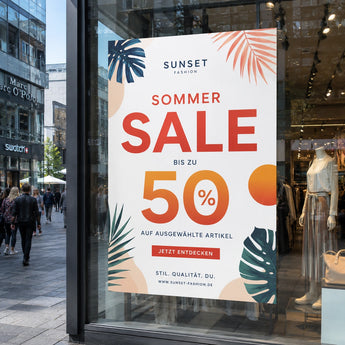 Poster drucken – ein großes Werbeplakat im Schaufenster eines Modegeschäfts, das mit sommerlichen Blattmotiven verziert ist und einen Sommer-Sale mit bis zu 50 % Rabatt ankündigt.