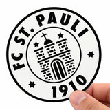 Eine Hand hält einen runden, schwarz-weißen Aufkleber mit dem Logo des FC St. Pauli. Das klassische Motiv zeigt den Vereinsnamen, das Gründungsjahr 1910 sowie eine stilisierte Burg mit Sternen. Ein ideales Beispiel für Sportvereine und Fanclubs, die ihre Wappen in hoher Qualität als eigene Sticker drucken lassen.