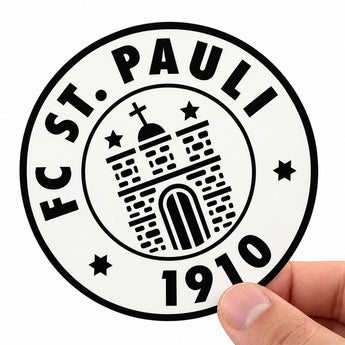 Eine Hand hält einen runden, schwarz-weißen Aufkleber mit dem Logo des FC St. Pauli. Das klassische Motiv zeigt den Vereinsnamen, das Gründungsjahr 1910 sowie eine stilisierte Burg mit Sternen. Ein ideales Beispiel für Sportvereine und Fanclubs, die ihre Wappen in hoher Qualität als eigene Sticker drucken lassen.