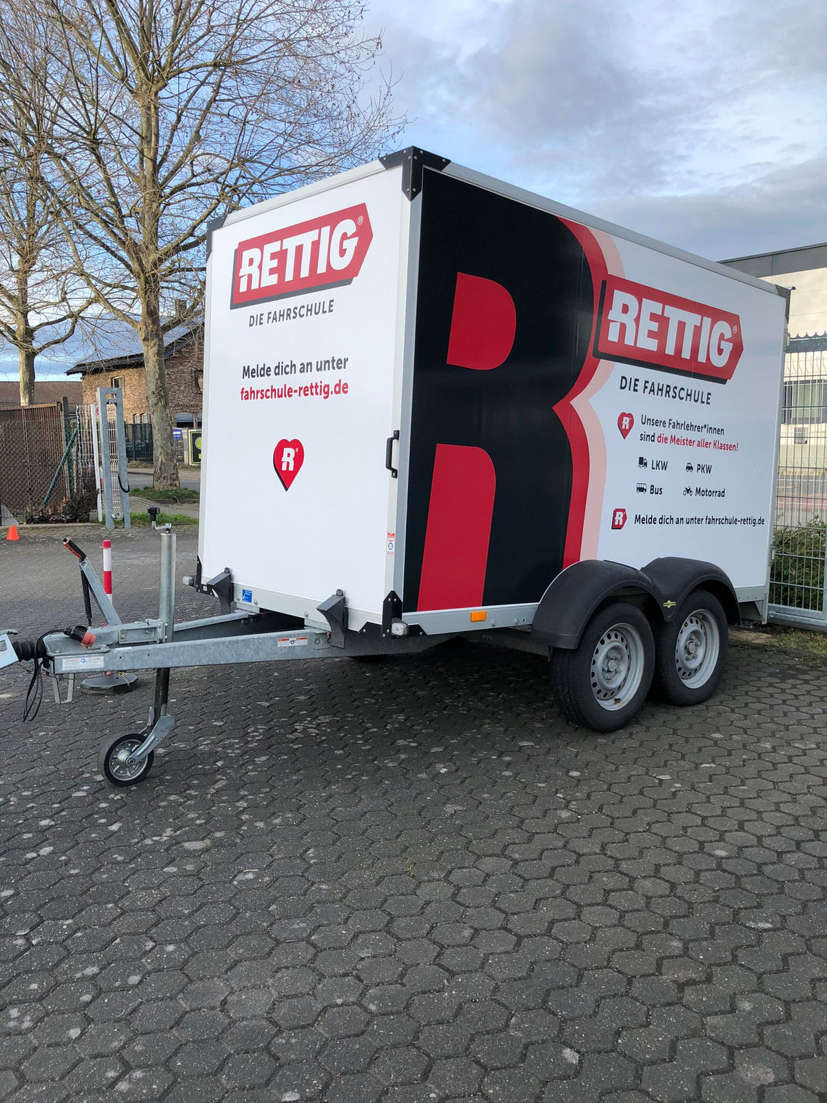 Werbefolierung eines Anhängers mit großem Rettig Fahrschule Logo und Informationen zu Führerscheinklassen als mobile Fahrzeugwerbung.