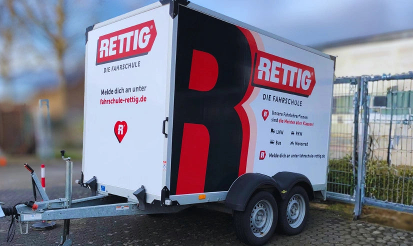 Werbefolierung eines Anhängers mit großem Rettig Fahrschule Logo und Informationen zu Führerscheinklassen als mobile Fahrzeugwerbung.