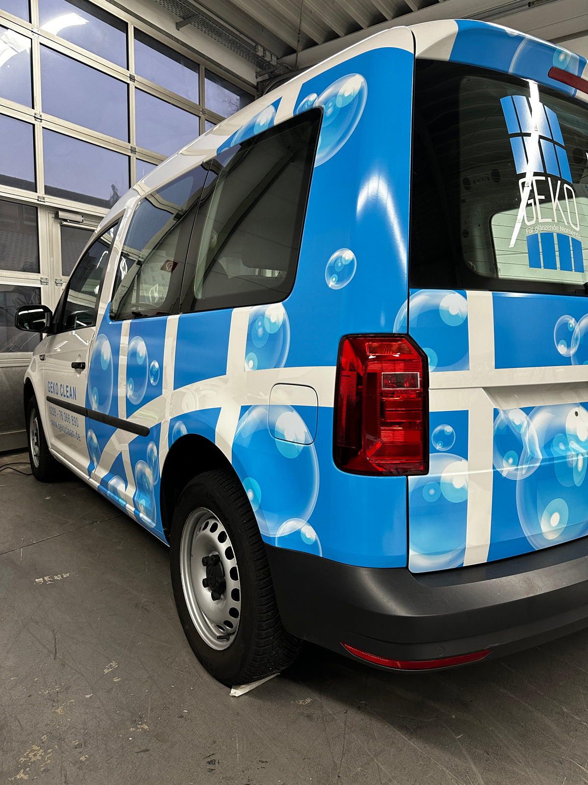 Teilfolierung eines weißen Transporters mit blauem Blasen-Design für eine Reinigungsfirma inklusive Firmenlogo und Werbegrafik auf der Fahrzeugseite.