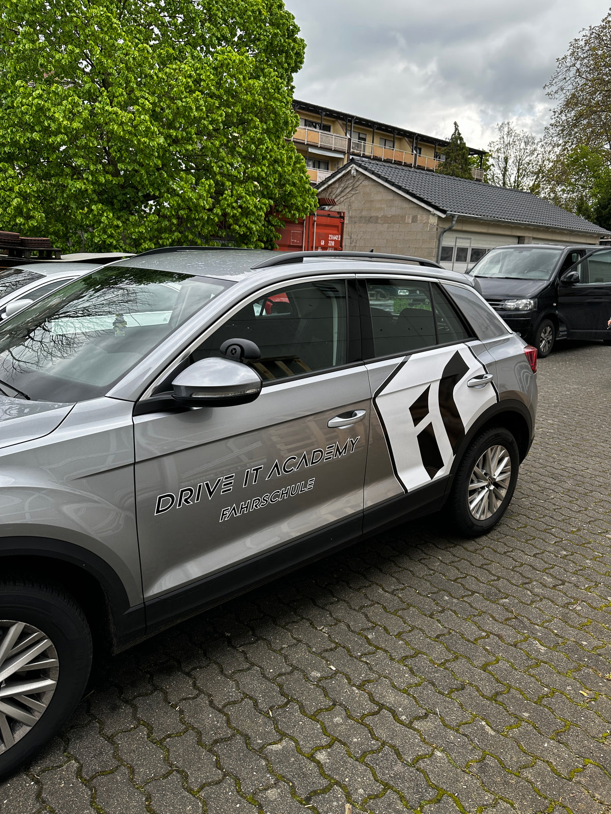 Fahrzeugbeschriftung eines Fahrschulautos mit Logo Drive It Academy und moderner Teilfolierung auf der Fahrzeugseite.