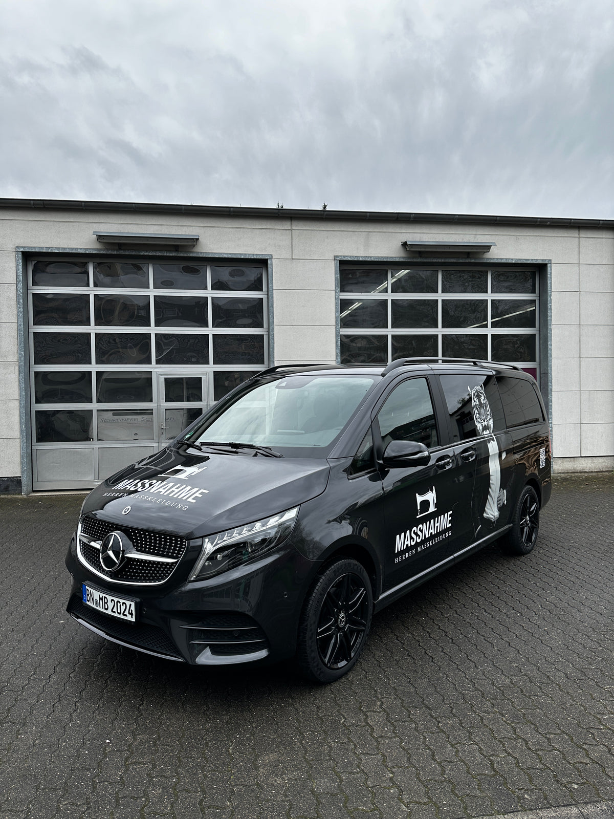 Fahrzeugbeschriftung auf einem schwarzen Transporter mit Logo und Schriftzug der Schneiderei Maßnahme auf der Fahrzeugseite und Motorhaube.