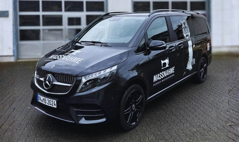 Fahrzeugbeschriftung auf einem schwarzen Transporter mit Logo und Schriftzug der Schneiderei Maßnahme auf der Fahrzeugseite und Motorhaube.
