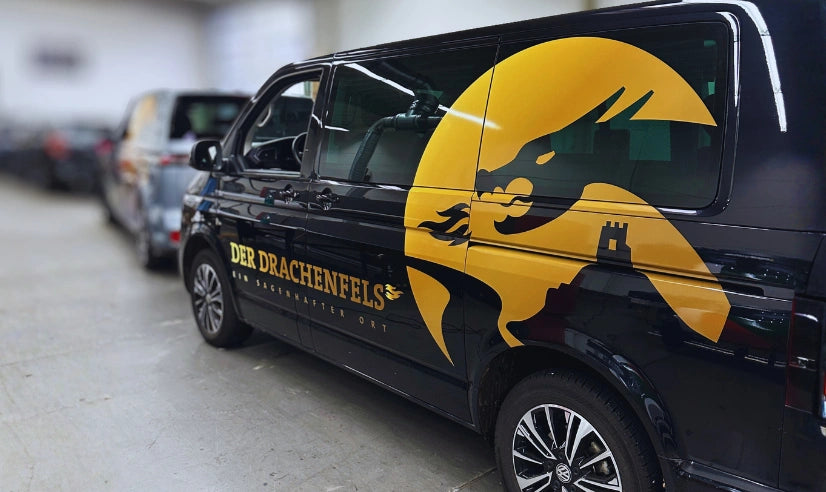 Fahrzeugbeschriftung eines schwarzen Transporters mit großer Drachenmotiv Teilfolierung und Logo Der Drachenfels auf der Fahrzeugseite.