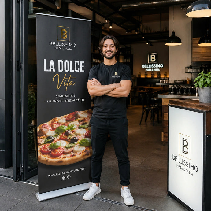 Ein lächelnder Gastronom steht neben einem schwarzen Gastro Werbeaufsteller mit Pizza-Motiv vor seiner Pizzeria.