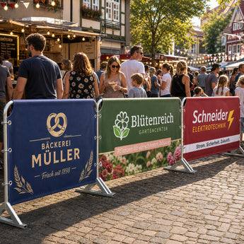 Hussen für Absperrgitter – verschiedene farbenfrohe Hussen für lokale Unternehmen wie Bäckereien und Gartencenter, die bei einem belebten Stadtfest an Absperrgittern befestigt sind.
