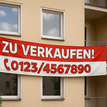 Ein rot-weißes "Zu Verkaufen" Werbebanner, das an einer Hausfassade hängt. Wir können auch Roll-Up Banner drucken.