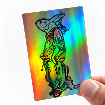 Eine Hand hält einen rechteckigen, holografischen Aufkleber mit starkem, regenbogenfarbenem Schimmer. Das als schwarze Linienzeichnung gedruckte Motiv zeigt einen Comic-Fisch im Streetwear-Look mit weiten Hosen, T-Shirt und Rucksack. Ein kreatives Beispiel dafür, wie Illustrationen wirken, wenn man sie als auffällige Sticker drucken lässt.