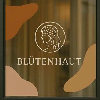 Transparente Fensteraufkleber mit Frauen-Logo und Schriftzug Blütenhaut auf einer Salon-Glasscheibe.