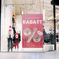 Transparente Fensteraufkleber als rosa Rabatt-Plakat mit Prozentzeichen im Schaufenster eines Modegeschäfts.