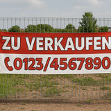 Ein rot-weißes "Zu Verkaufen" Werbebanner, das an einem Metallzaun befestigt ist. Wir können auch Roll-Up Banner drucken.